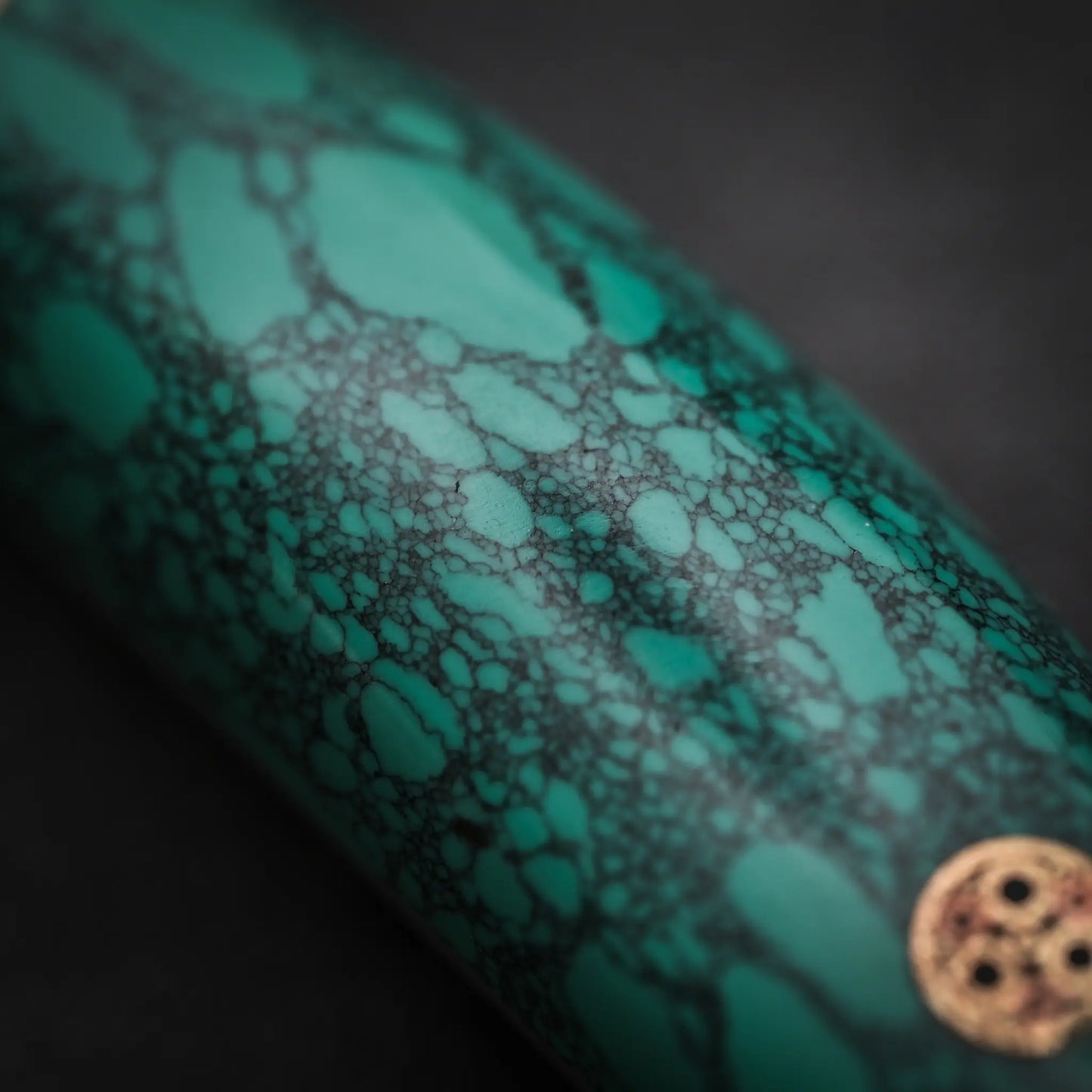 A close-up of the Nigara Hamono Nigara tsuchime SG2 kiritsuke nakiri 180mm shows its turquoise handle with dark, web-like veins and a gold circular accent, resembling the precise design of a Japanese vegetable knife, on a blurred dark background.