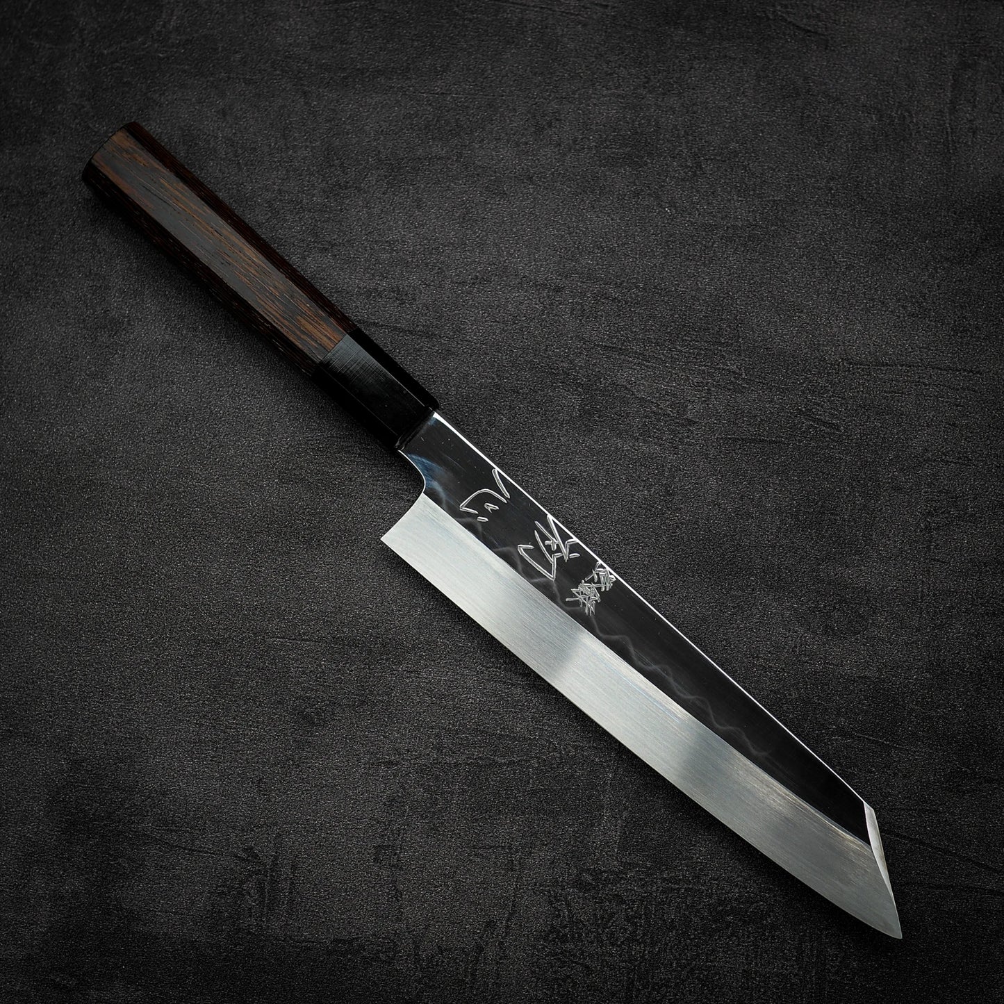 The Satoshi Nakagawa Nakagawa shirogami#3 honyaki kiritsuke gyuto 210mm features a dark wooden handle and shiny, angular blade, crafted with traditional Japanese techniques and resting on a dark textured surface.