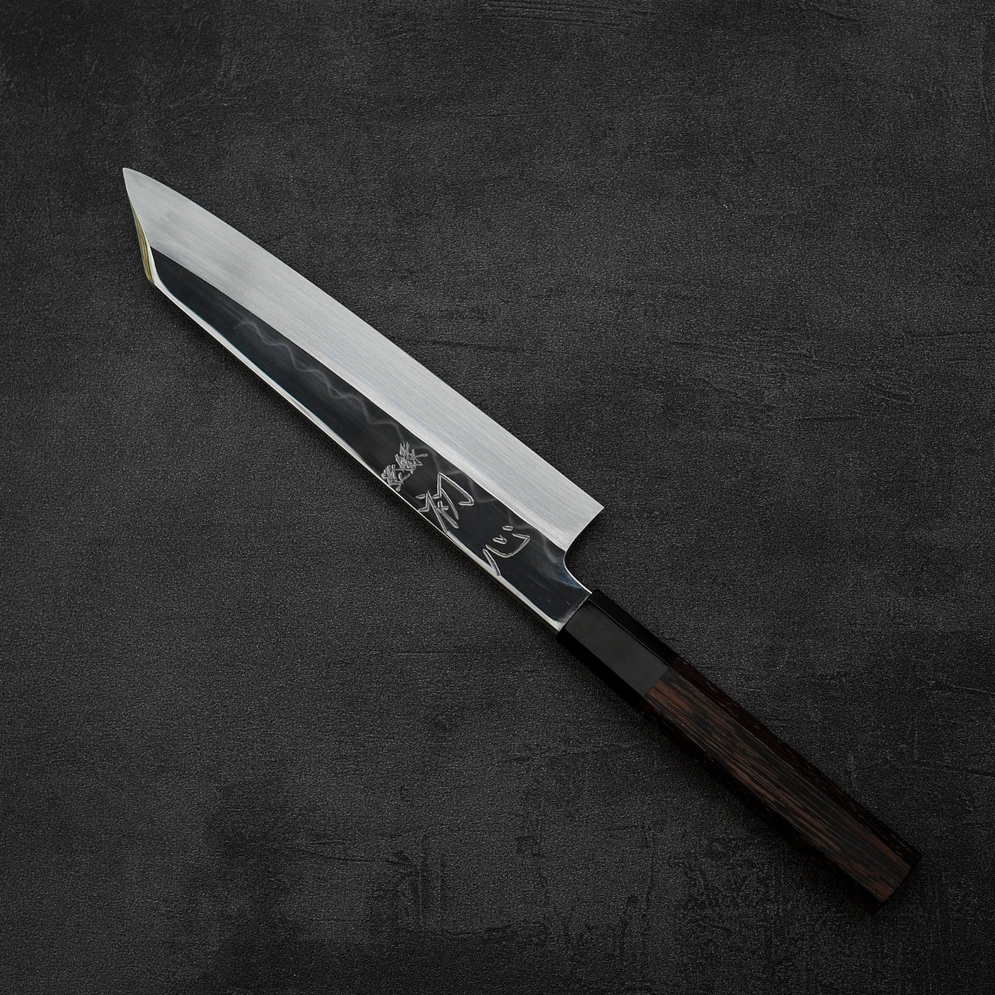 The Satoshi Nakagawa Nakagawa shirogami#3 honyaki kiritsuke gyuto 210mm features a sharp, pointed blade and dark wood handle, showcased on a textured black surface.