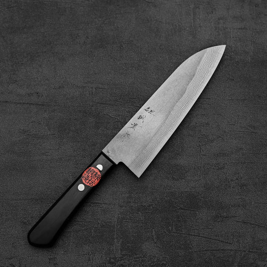 The Shigeki Tanaka nashiji damascus VG10 santoku kitchen knife by Shigeki Tanaka has a black handle and silver blade engraved with Japanese characters, shown on a dark textured surface.