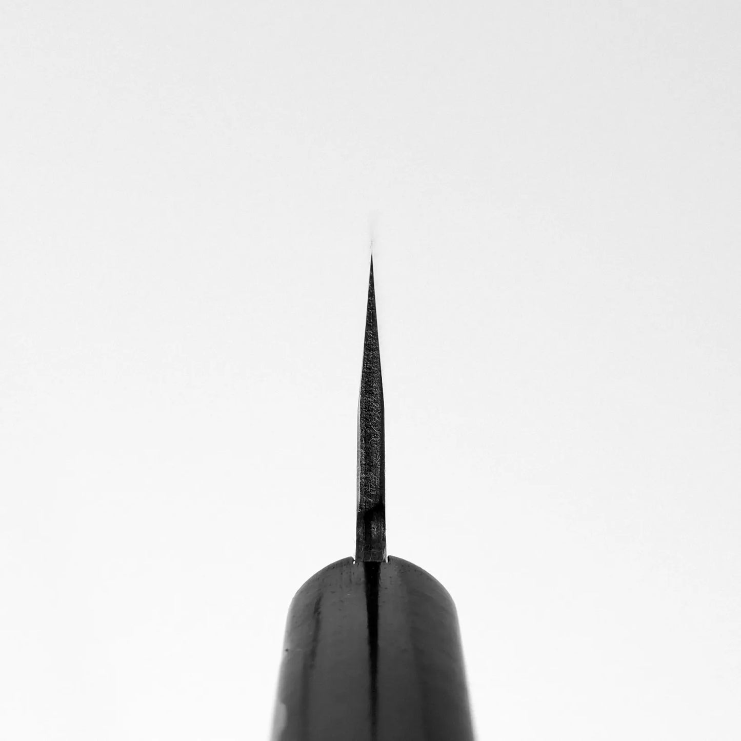 A close-up shows the pointed tip of a Shigeki Tanaka nashiji damascus VG10 santoku blade, viewed head-on and centered against a white background, with its sharp edge vertically aligned.
