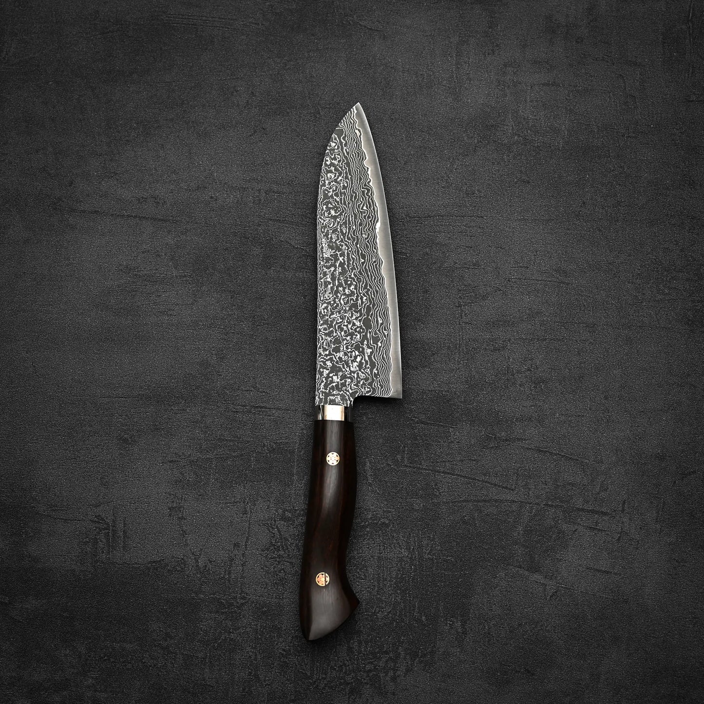 A Shigeki Tanaka R2 damascus santoku 170mm with an ironwood handle is placed on a dark textured surface.