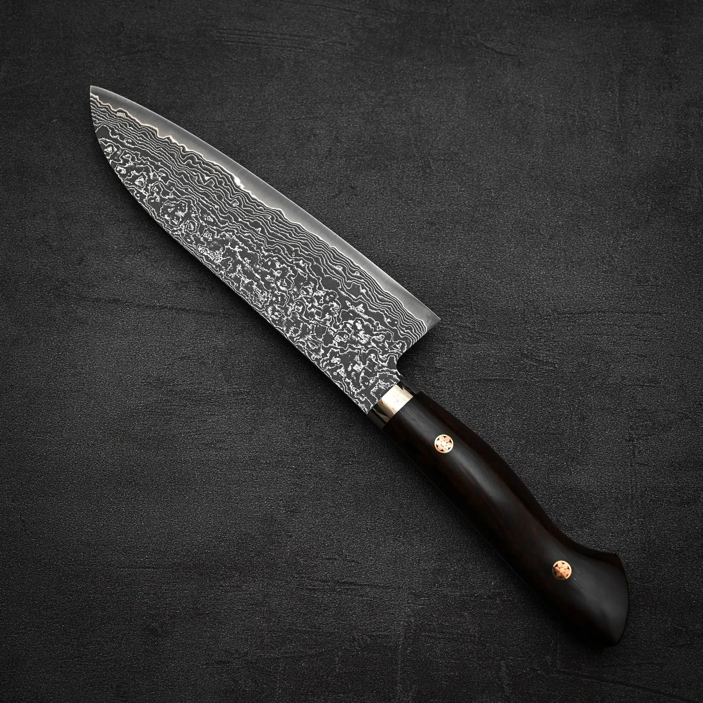 The Shigeki Tanaka R2 damascus santoku 170mm - ironwood by Shigeki Tanaka features a patterned R2 steel blade and an ironwood handle, displayed on a textured dark surface.
