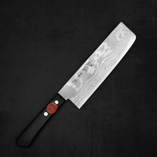 The Shigeki Tanaka VG10 damascus 165mm nakiri, with a damascus-patterned stainless steel blade and Japanese characters near the handle, lies on a dark textured surface.