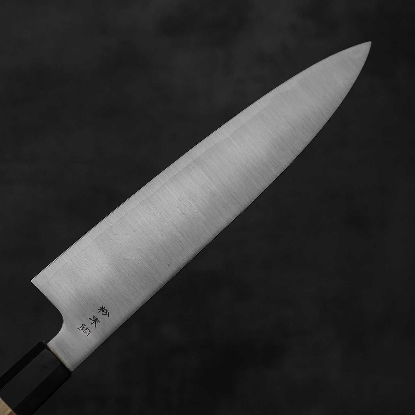 A close-up of the Sukenari SG2 240mm gyuto with magnolia saya, featuring a sharp blade and wooden handle, highlights the renowned Sukenari craftsmanship against a dark, blurred background.