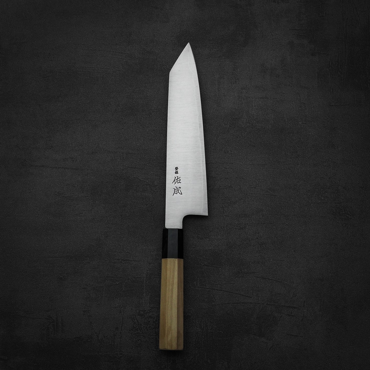 The Sukenari SG2 210mm kiritsuke gyuto chef knife features a wooden handle, sharp SG2 steel blade with Japanese engraving, and comes with a magnolia saya, set against a dark textured background.