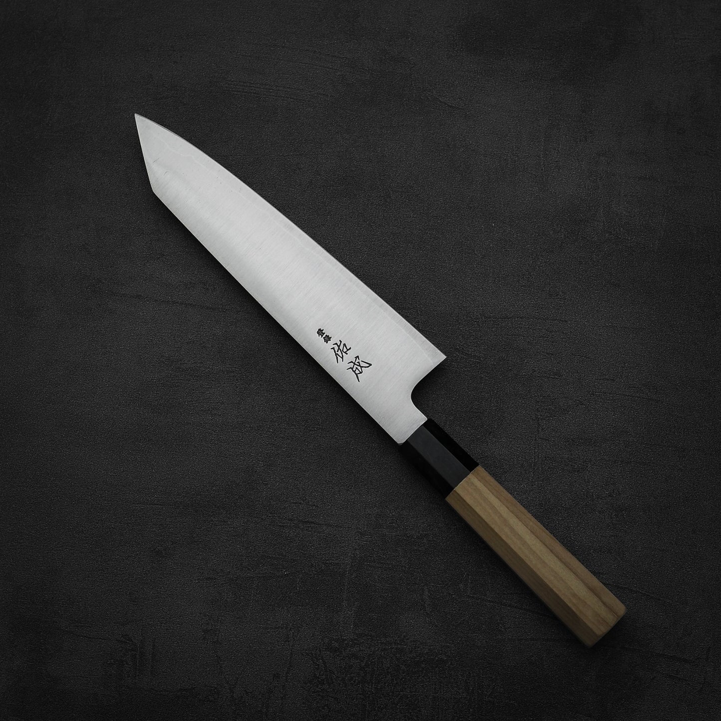 The Sukenari SG2 210mm kiritsuke gyuto features a shiny, pointed SG2 core steel blade, a light magnolia handle and saya, and engraved Japanese characters near the base. The knife is crafted by Sukenari for precision and style.