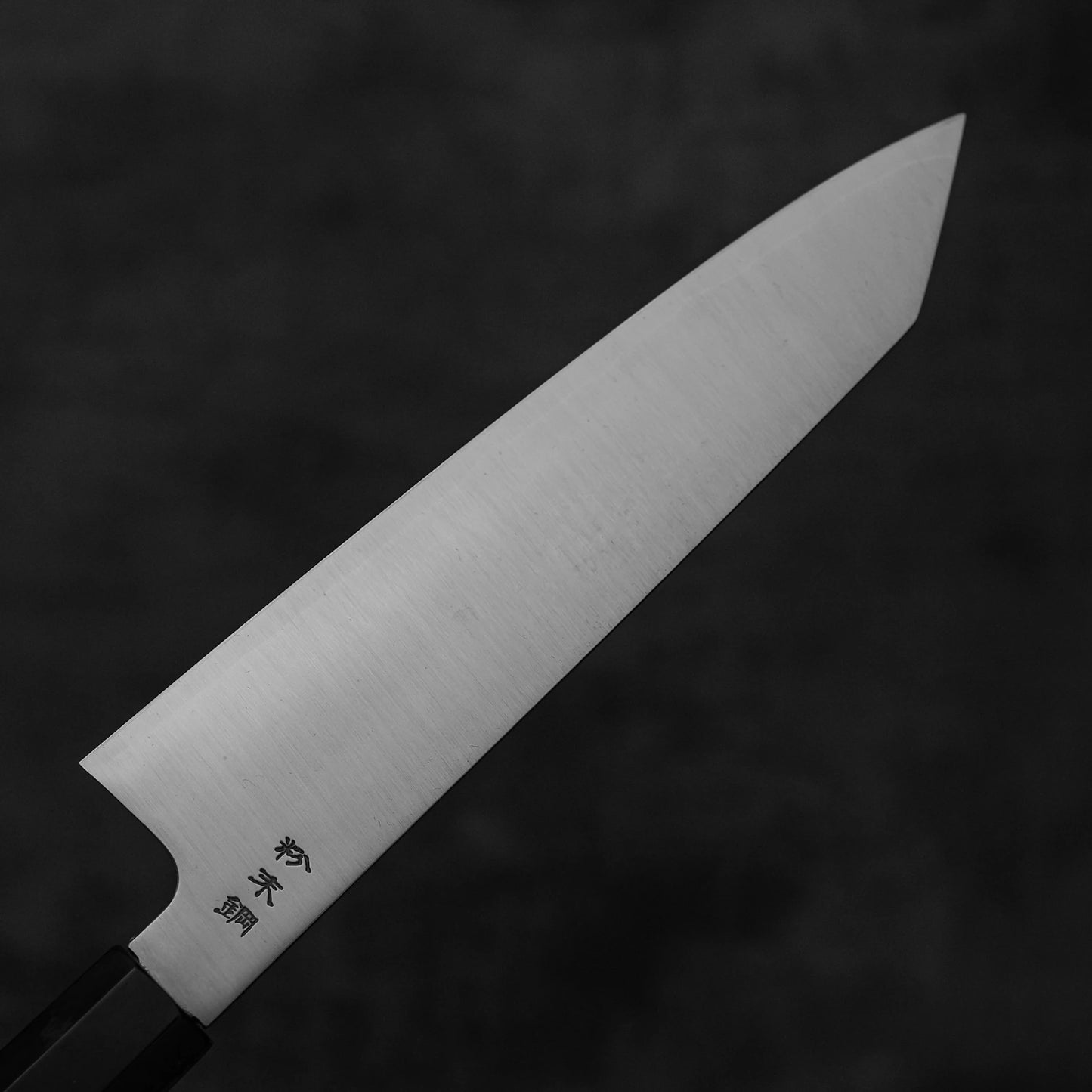 A close-up of the Sukenari SG2 210mm kiritsuke gyuto chef knife, featuring a sharp SG2 steel blade with Japanese engraving, a dark handle, and a magnolia saya, set against a dark, blurred background.