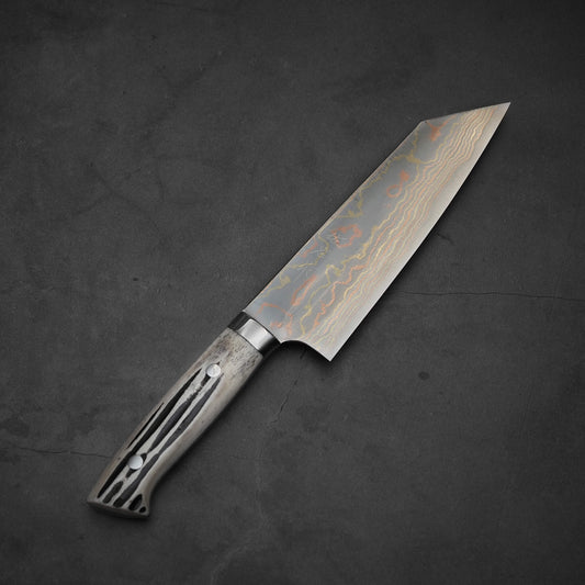 The Takeshi Saji rainbow damascus aogami#2 bunka 180mm with stag handle rests on a dark, slightly cracked surface.