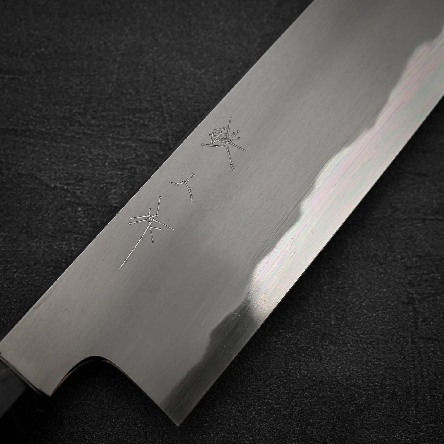 Close-up of the Tetsujin aogami#2 gyuto 240mm chefs knife by Tetsujin, featuring engraved Japanese characters on its polished blade, crafted from premium aogami#2 steel and resting on a dark textured surface.