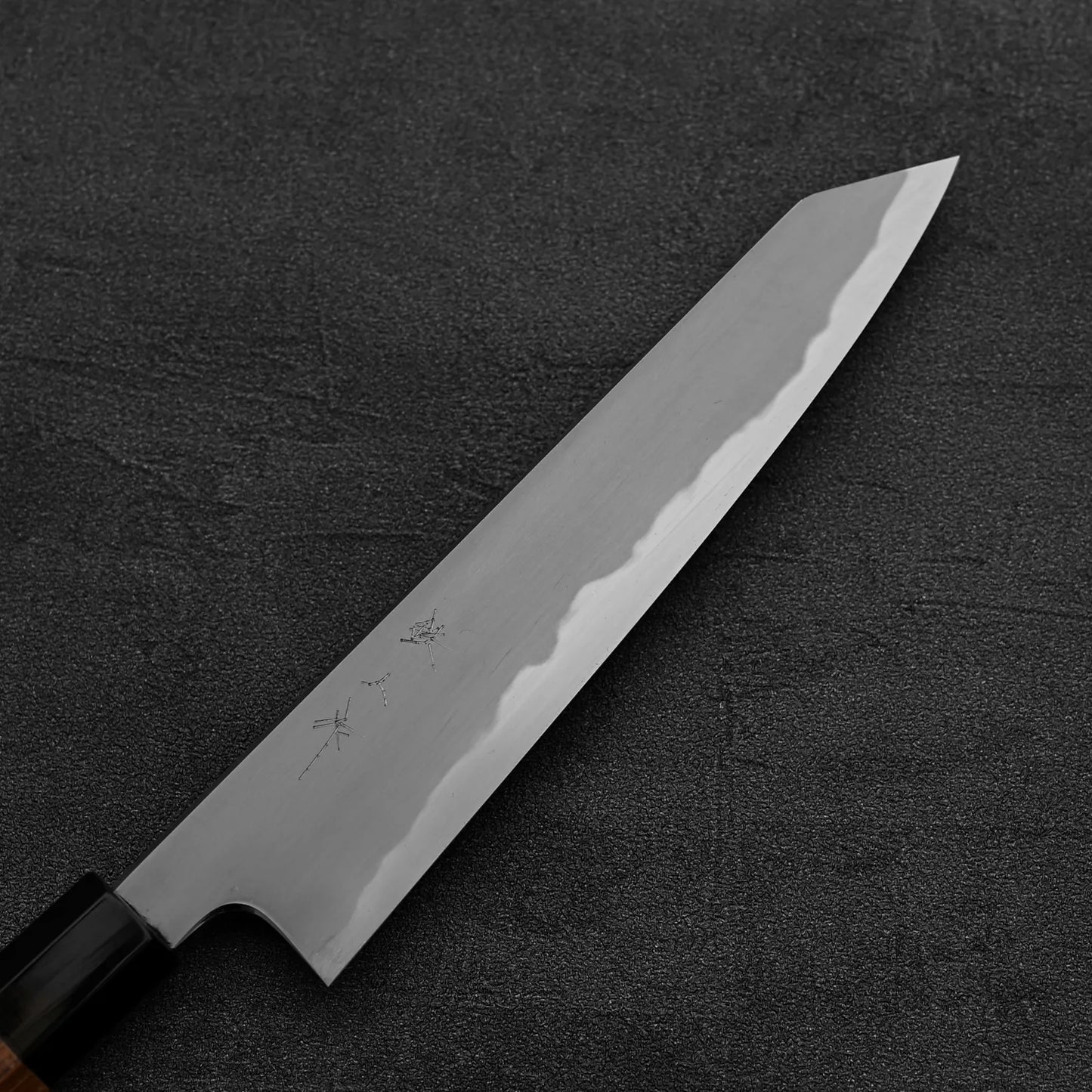 The Tetsujin kasumi aogami#2 petty knife 165mm, featuring a sharp, angular blade with a kasumi finish and subtle markings on its aogami#2 steel near the wooden handle, rests on a dark textured surface.