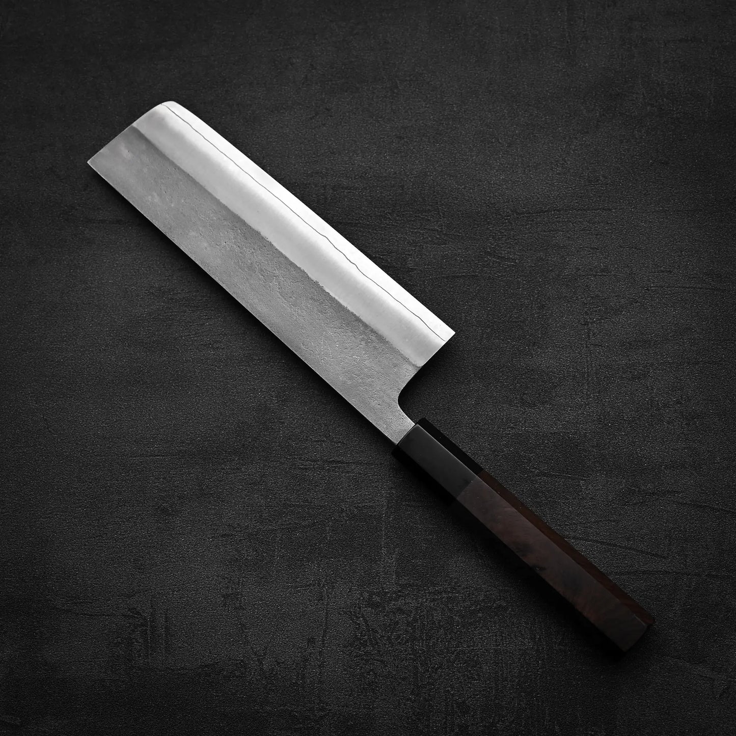 A Yoshikane Hatsukokoro x Yoshikane nashiji SKD nakiri 165mm, a Japanese knife with a rectangular blade and wooden handle, is placed on a dark textured surface.