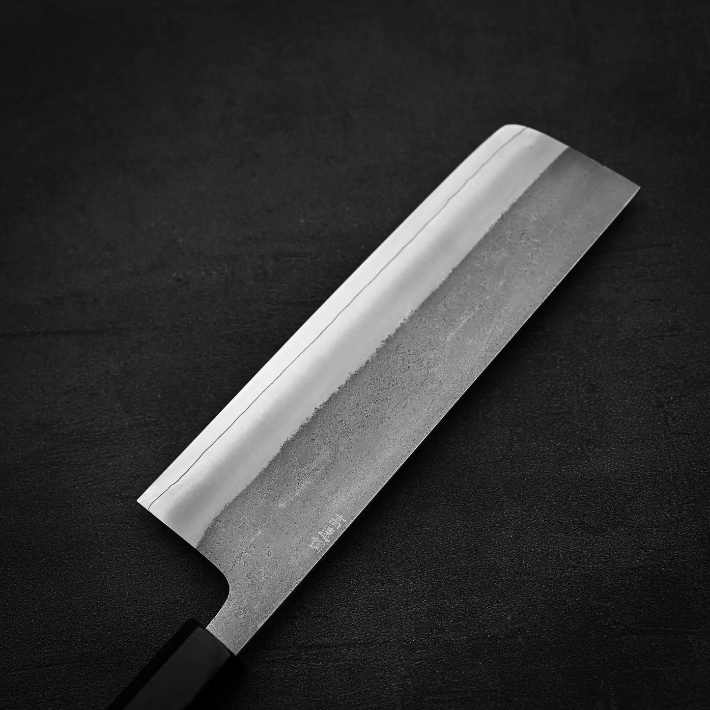 The Hatsukokoro x Yoshikane nashiji SKD nakiri 165mm by Yoshikane features a rectangular blade with a visible hamon line and subtle lower texture, presented on a dark, textured surface.