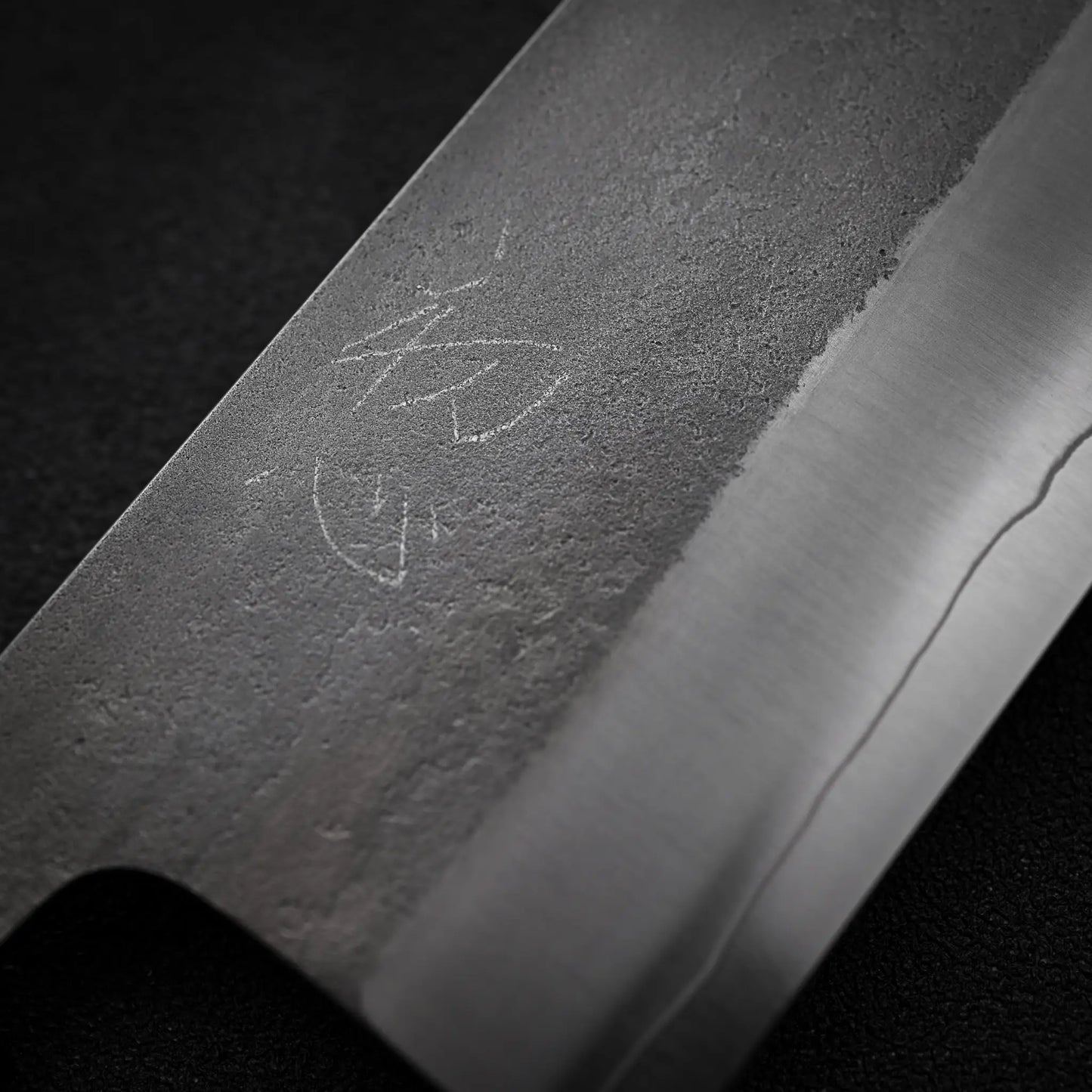 Close-up of the Hatsukokoro x Yoshikane nashiji SKD nakiri 165mm blade by Yoshikane, highlighting the textured nashiji finish and detailed etching, set against a dark background.