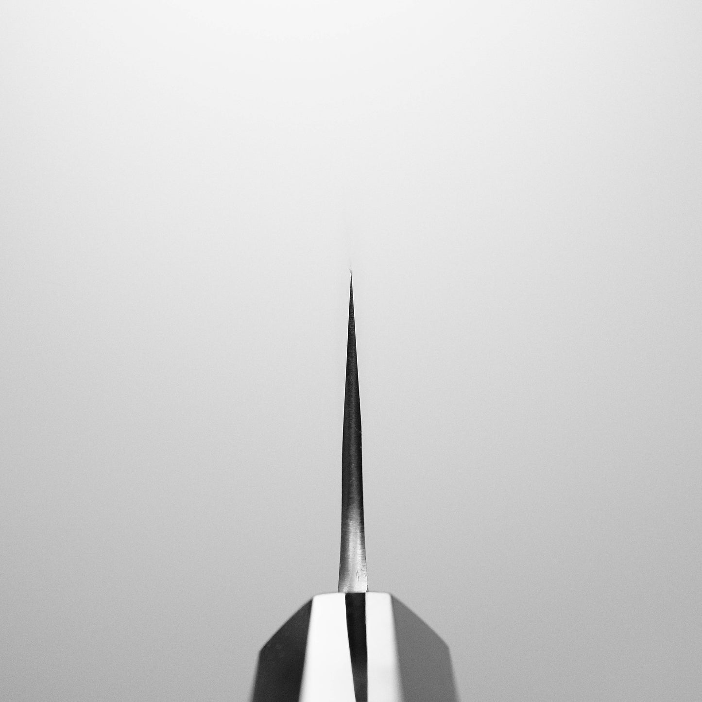 Close-up of the Yoshikane nashiji shirogami#2 gyuto 240mm knife’s sharp tip, showcased vertically against a plain light gray background.