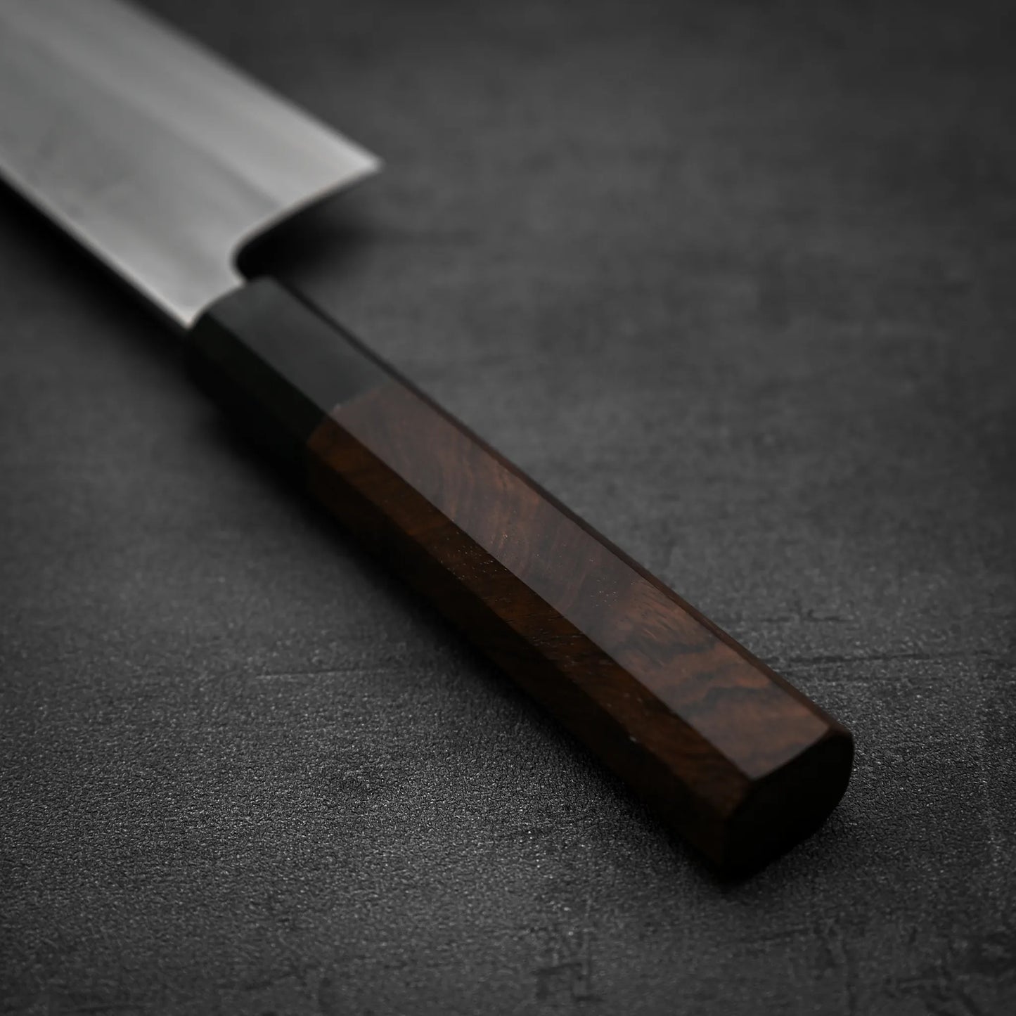 Close-up of the Yoshikane Hatsukokoro x Yoshikane nashiji shirogami#2 kiritsuke gyuto 210mm, featuring a wooden handle and stainless steel blade with an elegant nashiji finish, displayed on a dark textured surface.