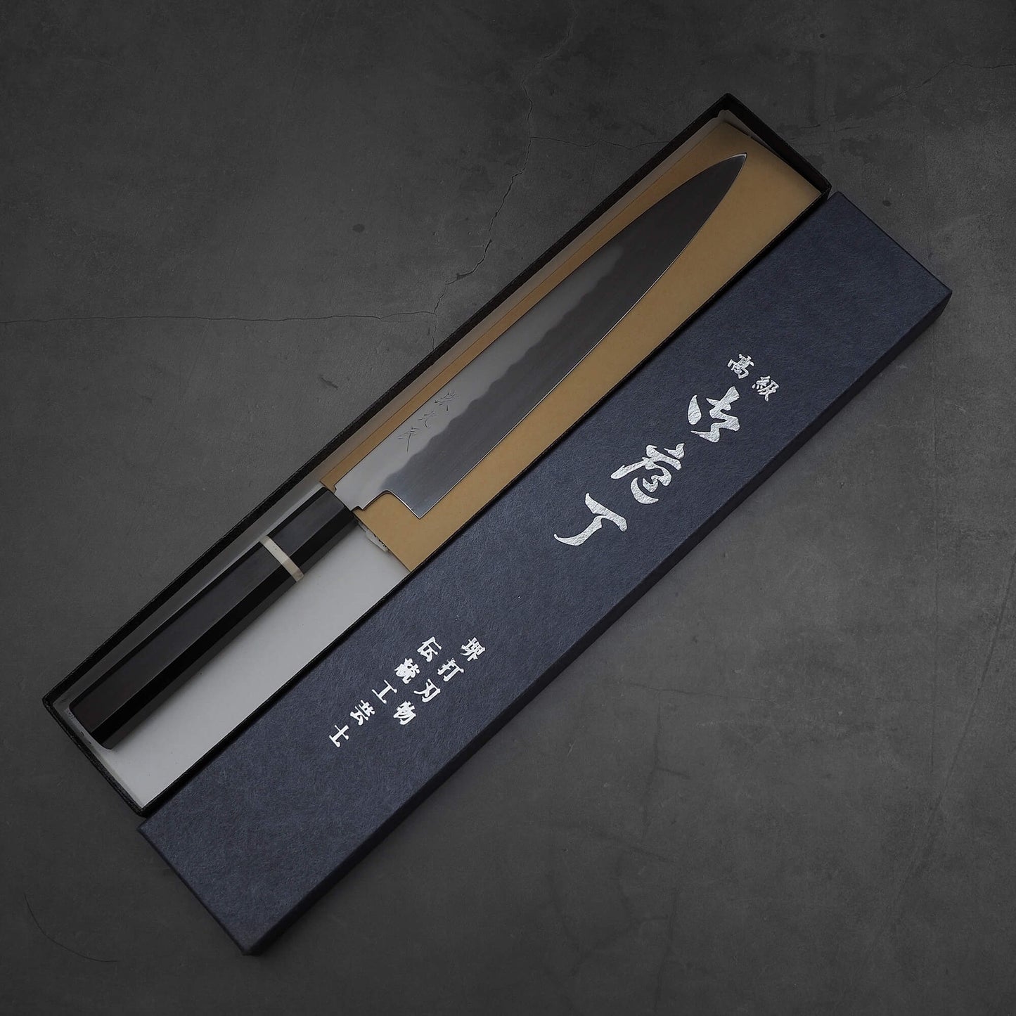 Top down view of Yoshikazu Ikeda honyaki sujihiki. This hand-forged Japanese knife is made of shirogami#3 steel. Knife is inside its box