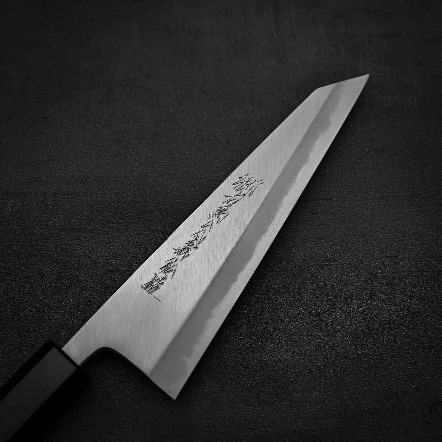 The Yoshikazu Tanaka shirogami#1 double bevel honesuki 170x50, featuring engraved kanji on the blade, is displayed on a dark textured surface.