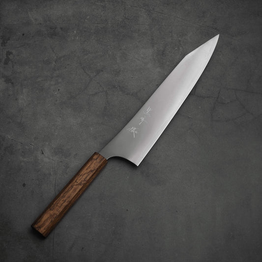 The Yu Kurosaki HAP40 Gekko kiritsuke gyuto 240mm chef’s knife, featuring a wooden handle and an engraved sharp HAP40 steel blade, is displayed on a dark gray textured surface.
