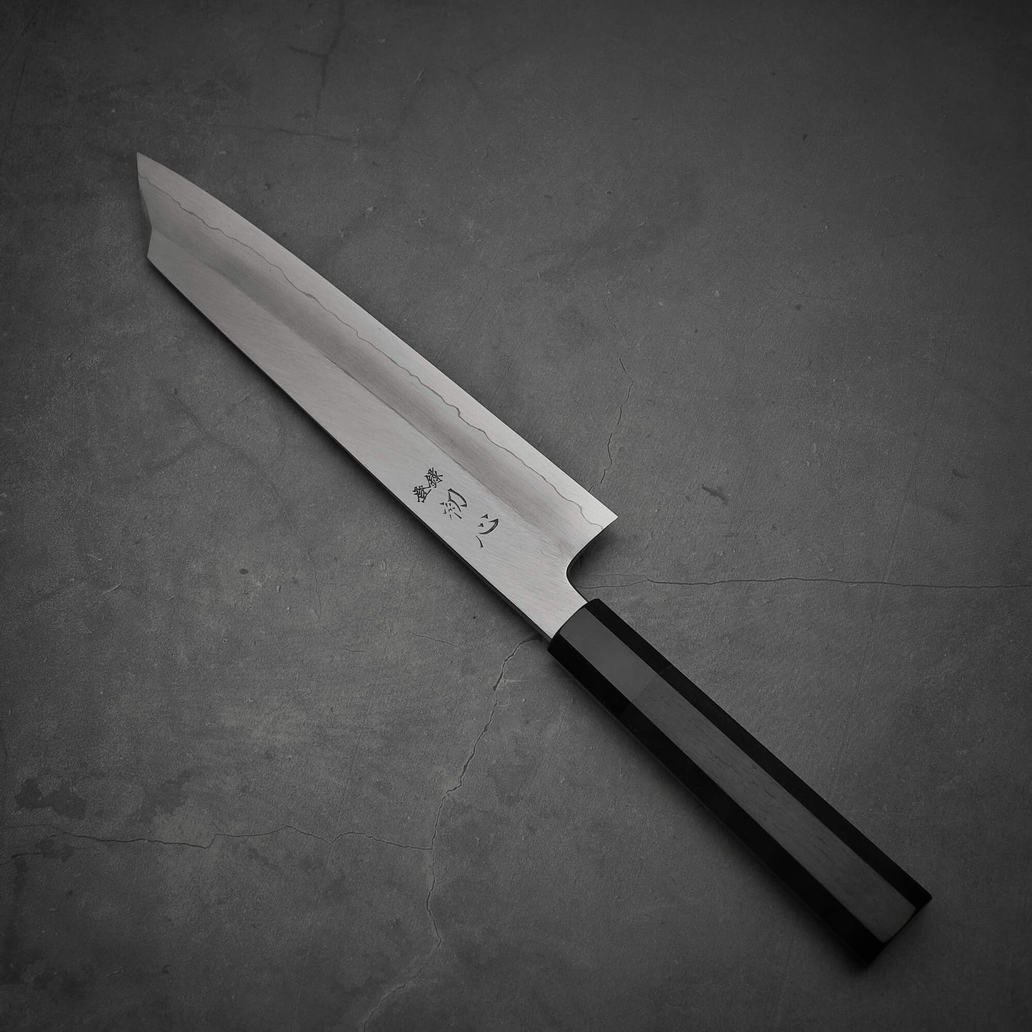 Top view of Hatsukokoro Nakagawa ginsan kiritsuke gyuto knife where pointed tip is facing towards upper left