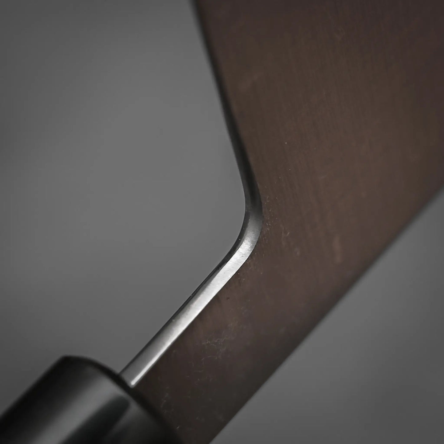Close-up of the joint between blade and handle of the Masamoto KS gyuto 210mm, showing a smooth transition and sharp edge with a matte Shirogami#2 steel finish. The Masamoto knife is set against a blurred gray background.