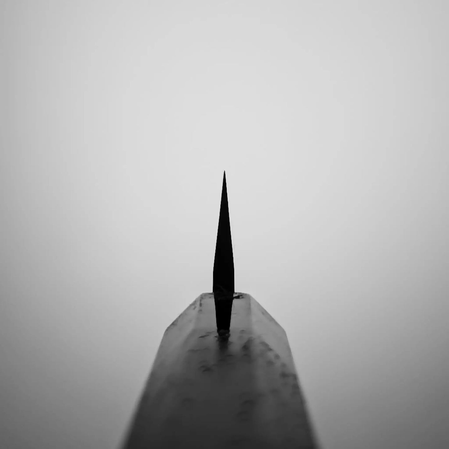 A black-and-white close-up shows the Nigara Hamono Nigara kurozome ginsan damascus kiritsuke petty knife 150mm, its Damascus blade pattern, reminiscent of a Japanese knife, sharply in focus and centered against a blurred background.