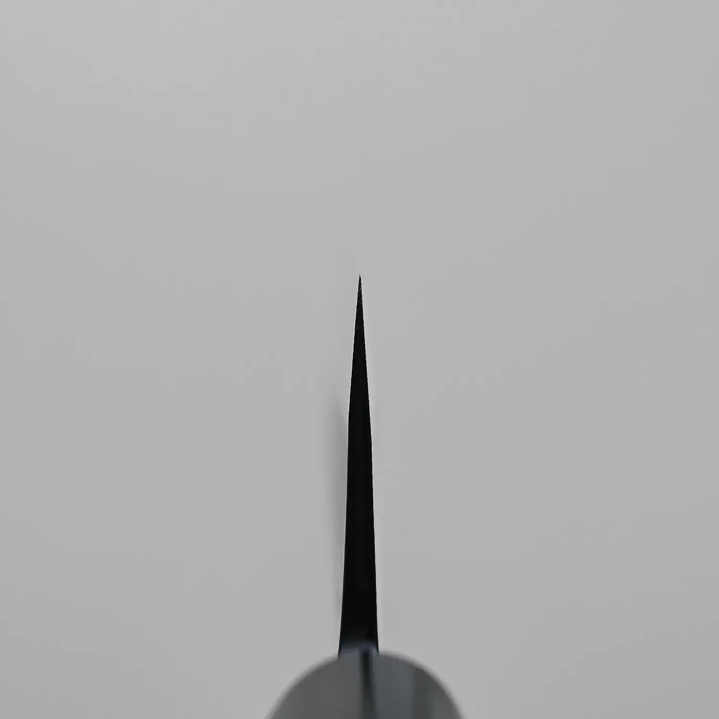 A close-up, top-down view of the choil shot of an Ohishi kurouchi SLD gyuto 210mm knife blade, centered vertically against a plain, light gray background.