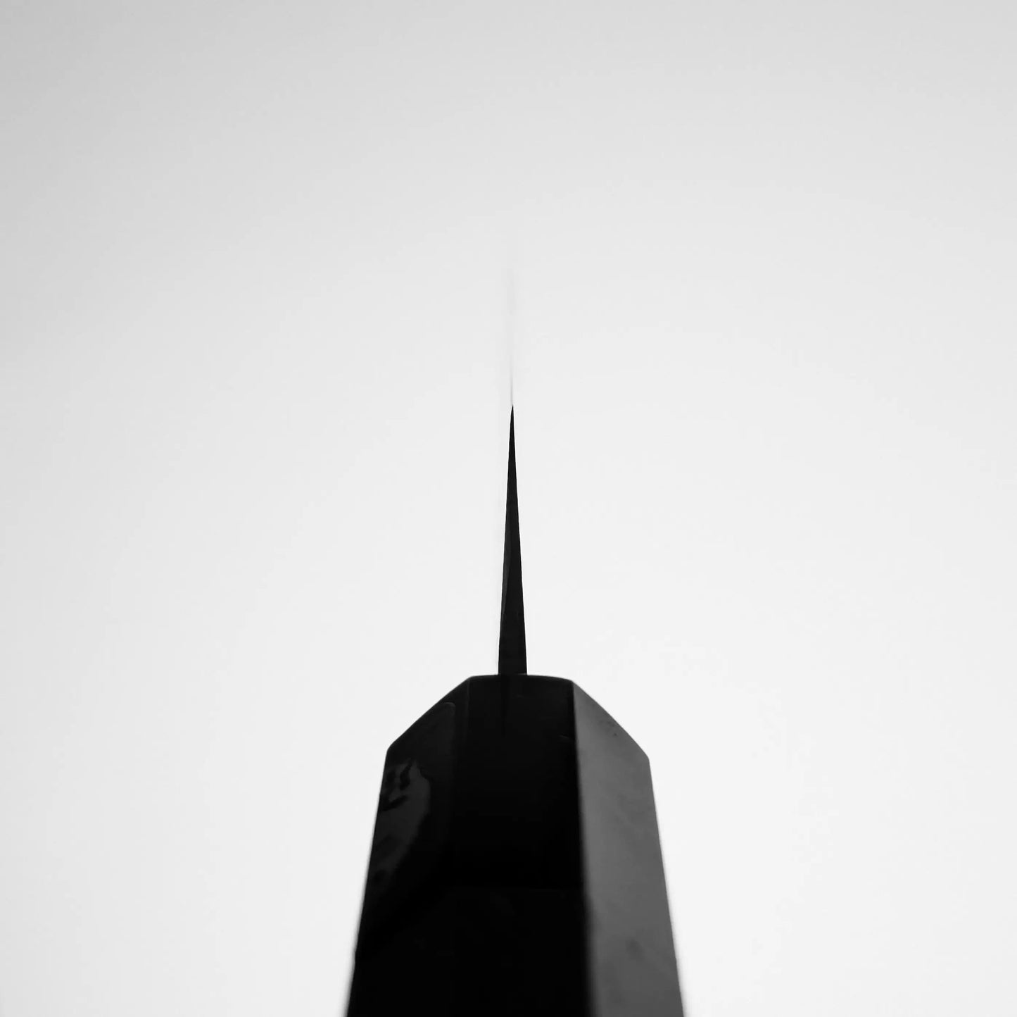 A close-up, upward view of a pointed skyscraper spire against an overcast sky, its sleek form reminiscent of the precision and artistry found in a Shigeki Tanaka aogami#2 damascus petty knife.