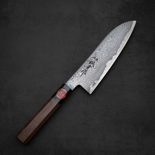 The Shigeki Tanaka R2 damascus santoku 170mm features a patterned blade, wooden handle, and Japanese characters engraved on the steel, shown resting on a dark textured surface.