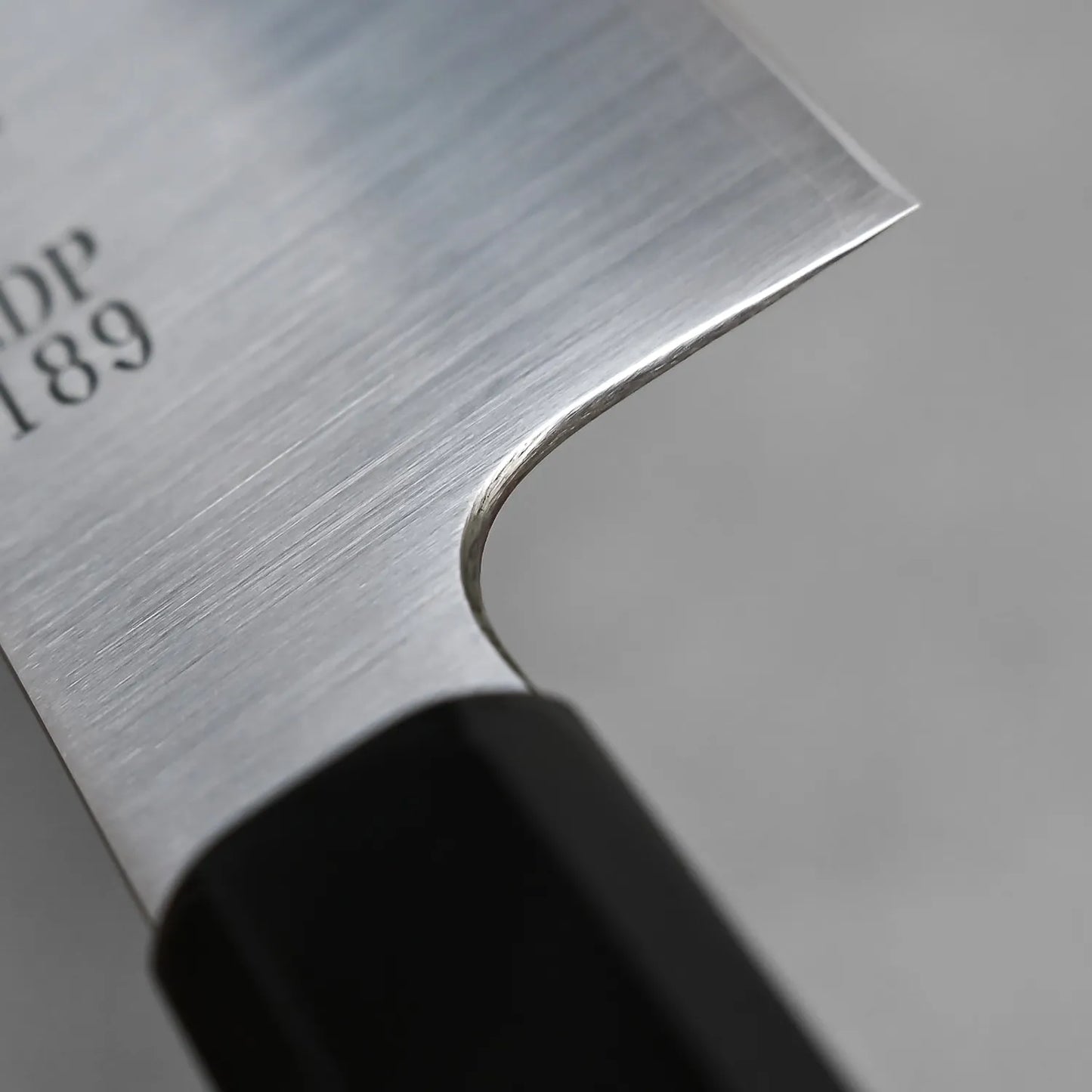A close-up of the Sukenari ZDP189 gyuto 210mm knife highlights its sharp edge, smooth bolster, and partial engraved number on the ZDP189 steel blade.