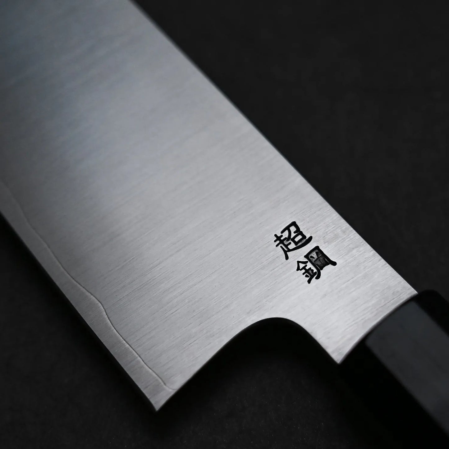 Close-up of the Sukenari ZDP189 kiritsuke gyuto 270mm, a Japanese kitchen knife by Sukenari with outstanding edge retention, a sharp ZDP189 stainless steel blade, black handle, and two kanji characters engraved near the base.