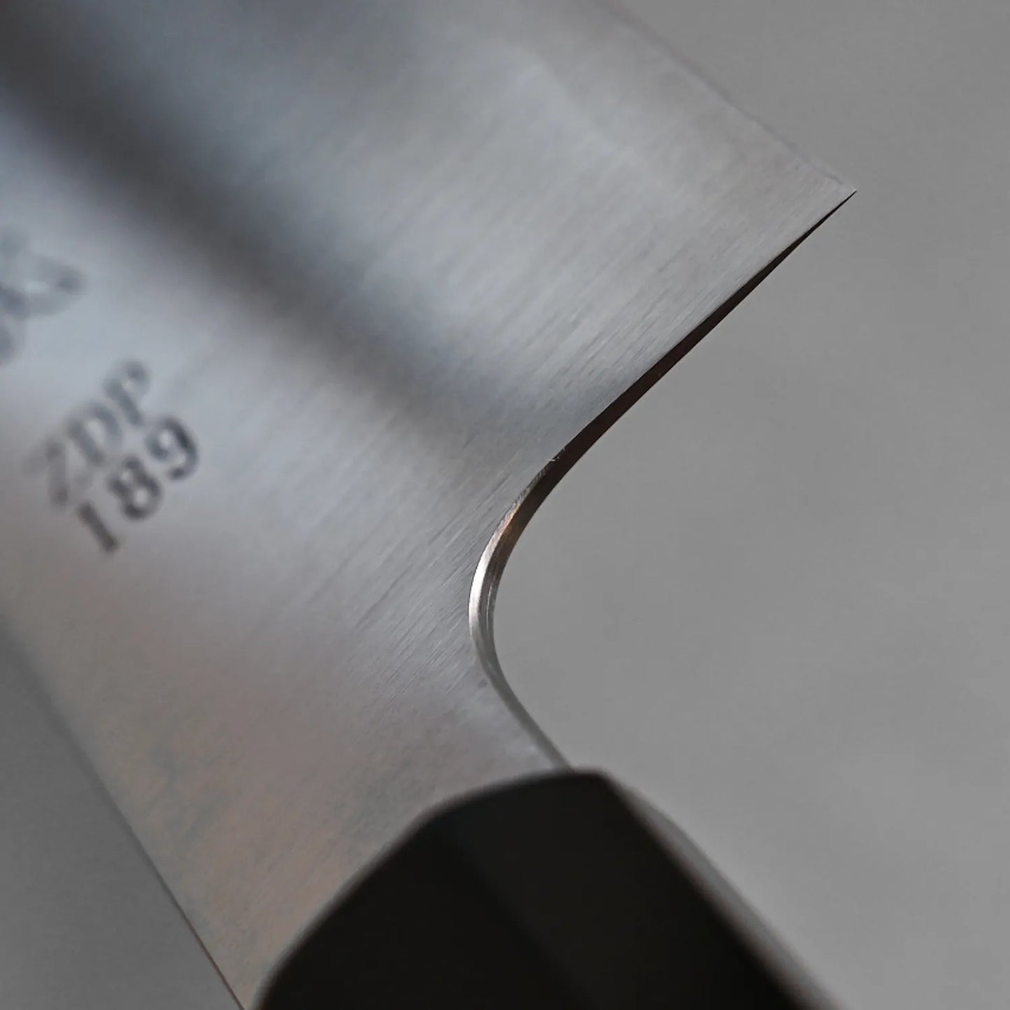 Close-up of the Sukenari ZDP189 kiritsuke gyuto 270mm blade, showing its sharp edge, outstanding edge retention, and subtle ZDP189 engraving near the top left. The image also partially reveals the Sukenari handle.