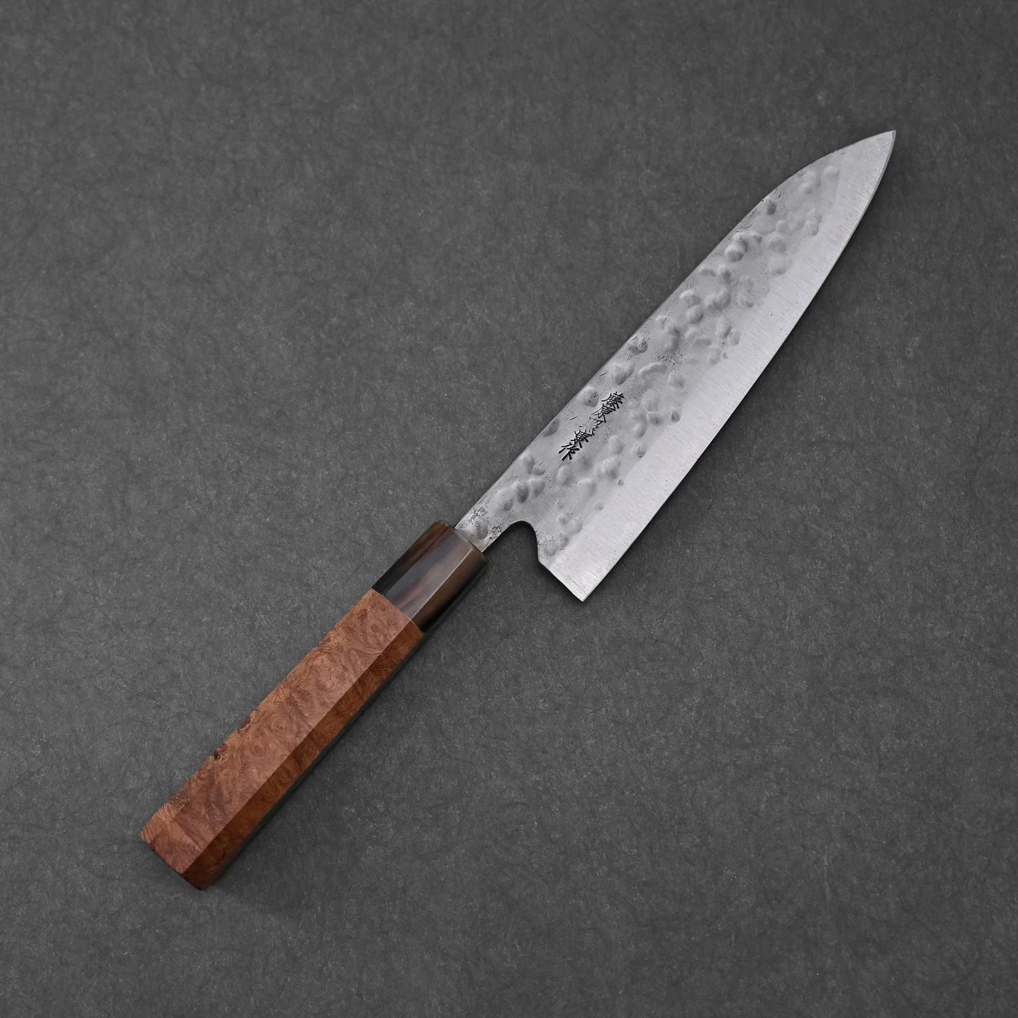 A Teruyasu Fujiwara Maboroshi shirogami#1 wa-gyuto 210mm with custom handle and saya, featuring a polished choil, lies diagonally on a dark textured surface.