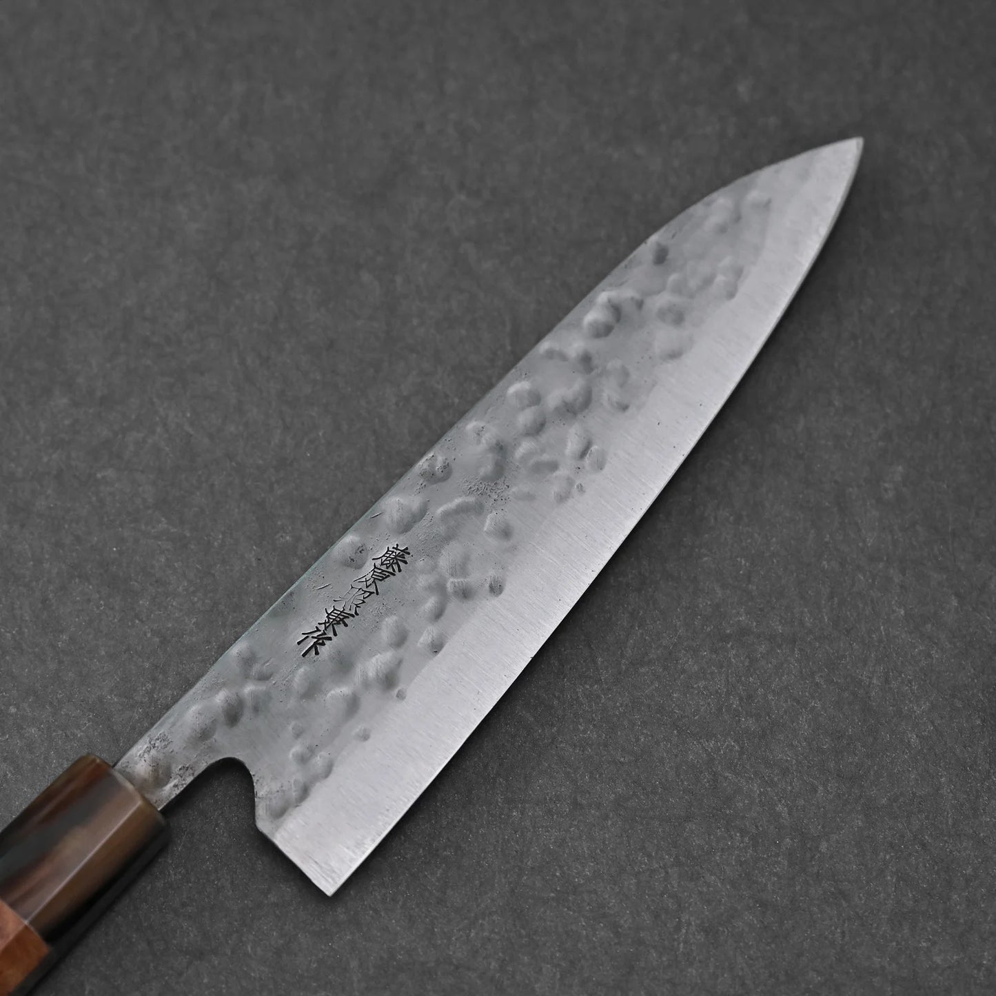 A Teruyasu Fujiwara Maboroshi shirogami #1 wa-gyuto 210mm with custom handle and saya, featuring a polished choil, rests on a dark grey textured surface. Engraved markings are visible near the handle.