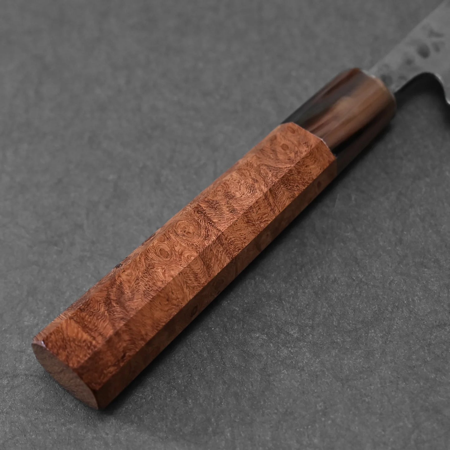 A close-up of the Teruyasu Fujiwara Maboroshi shirogami#1 wa-gyuto 210mm, featuring its custom wood handle with polished grain and rectangular shape, shown on a dark textured background.
