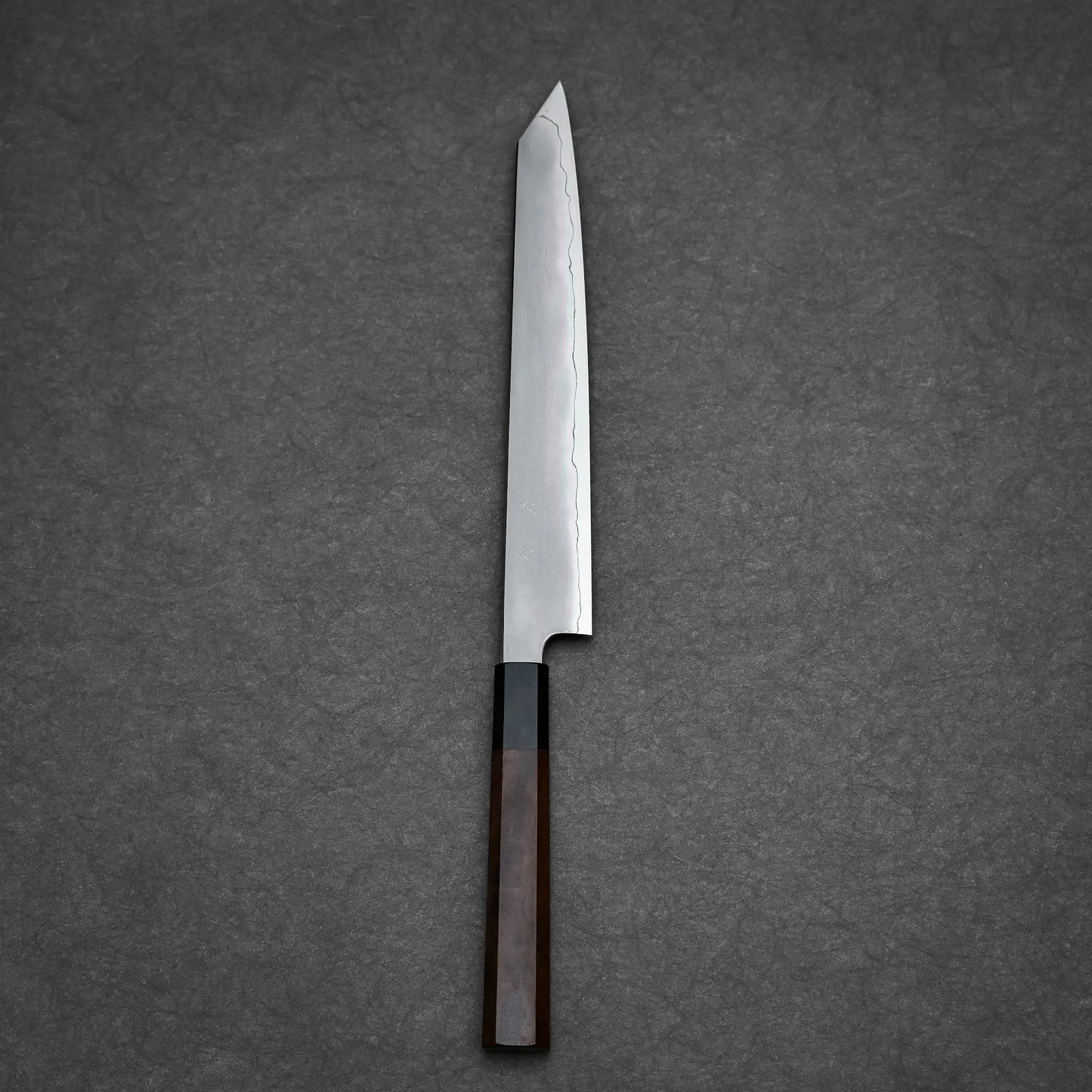 The Tetsujin kasumi ginsan kiritsuke sujihiki 240mm, by Tetsujin, features a straight-edge Ginsan steel blade with a kasumi finish and pointed tip, paired with a dark wooden handle and displayed on a textured gray surface.