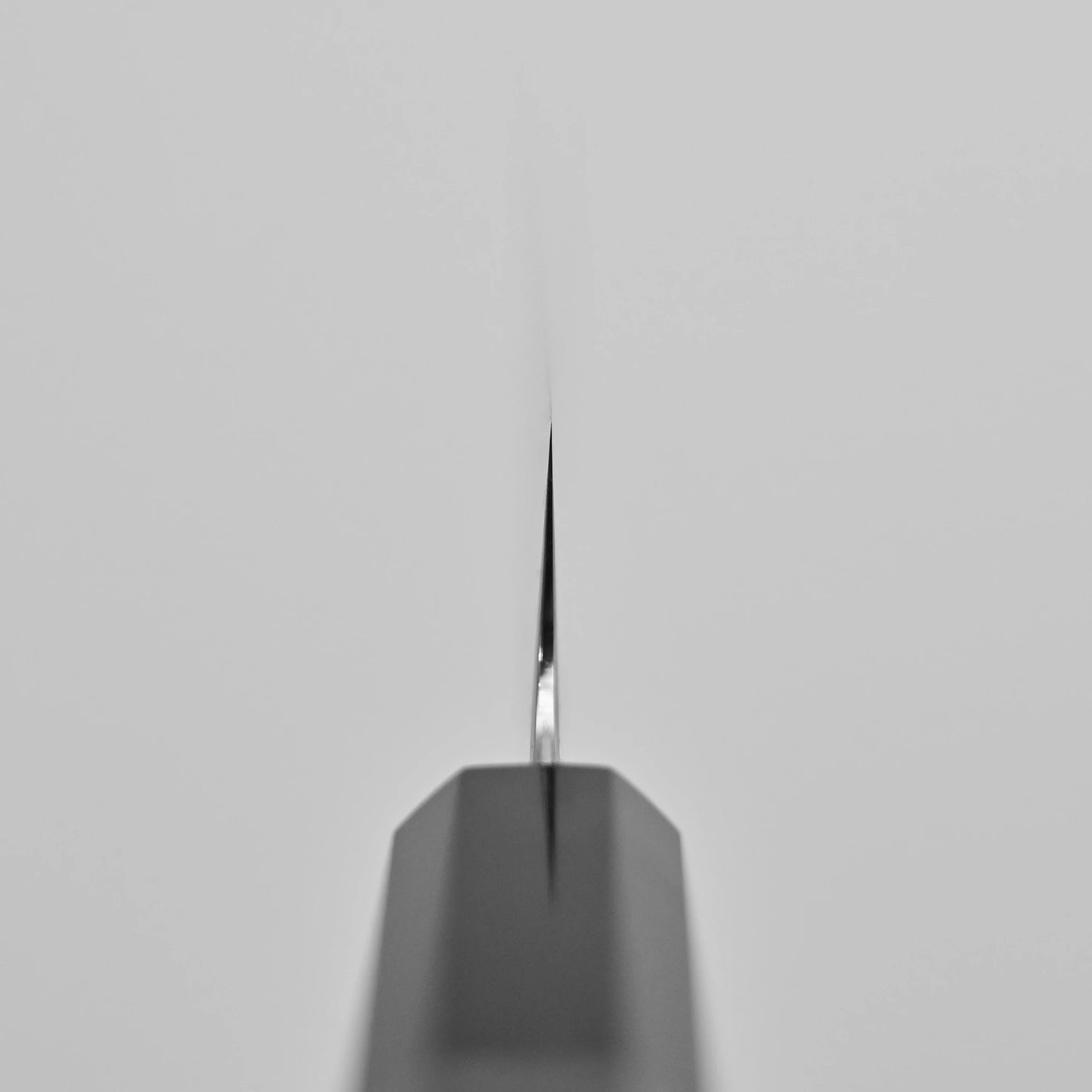 Close-up of the Tetsujin kasumi ginsan kiritsuke sujihiki 240mm tip, viewed from above to show its sharp, thin edge and kasumi finish, centered on a plain light gray background.