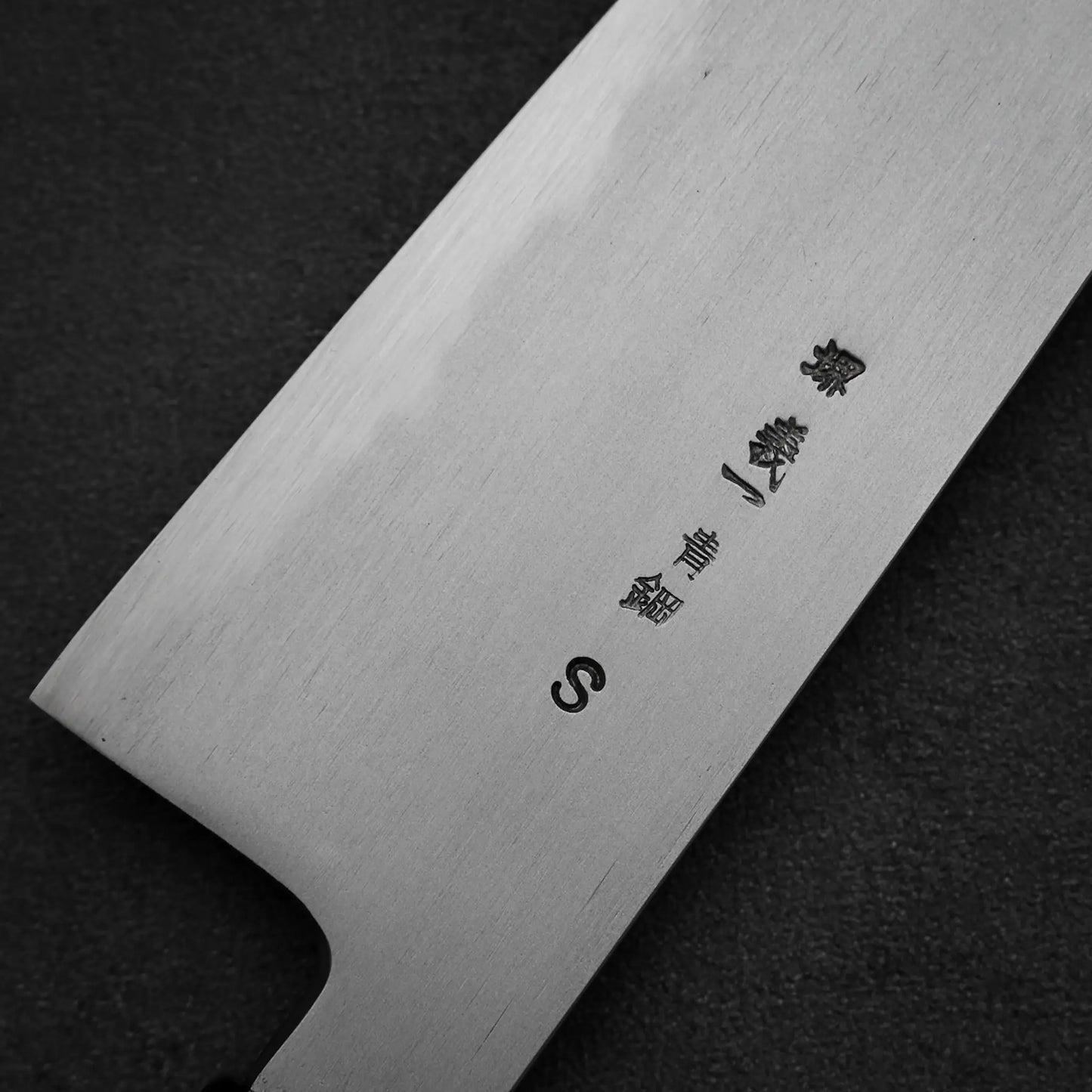 A close-up of the Yoshikazu Tanaka AS tall gyuto 210mm showcases its blade with Japanese characters and the letter S, forged from Aogami Super steel, set against a dark background.