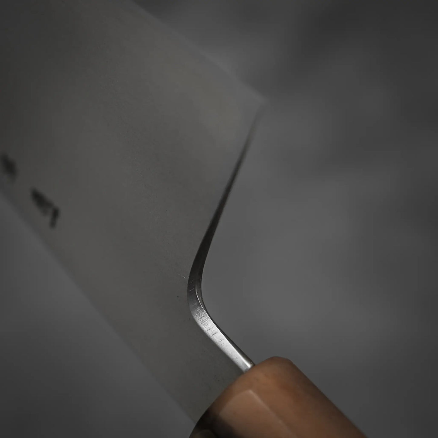 Close-up of the blade and wooden handle of the Yoshikazu Tanaka AS tall gyuto 240mm knife, set against a plain, dark background.