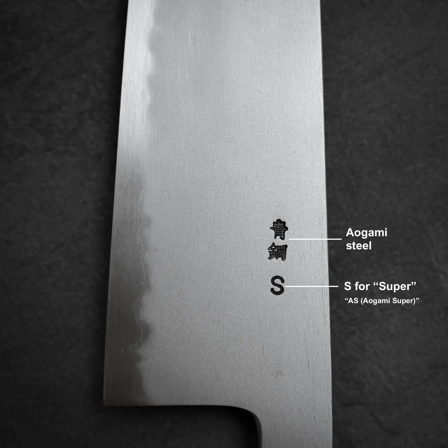 Close-up of the Yoshikazu Tanaka AS tall gyuto 240mm blade, showing engraved Aogami Super steel characters against a dark background.