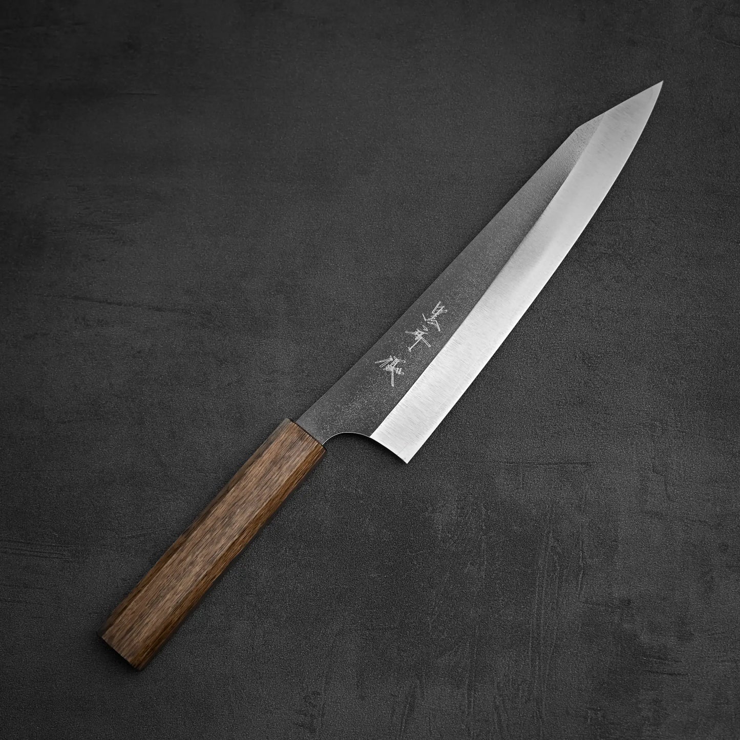 The Yu Kurosaki Gekko VG-XEOS kiritsuke gyuto 210mm, featuring a sharp VG-XEOS blade and wooden handle, lies diagonally on a dark textured surface with elegant Japanese characters engraved on the blade.