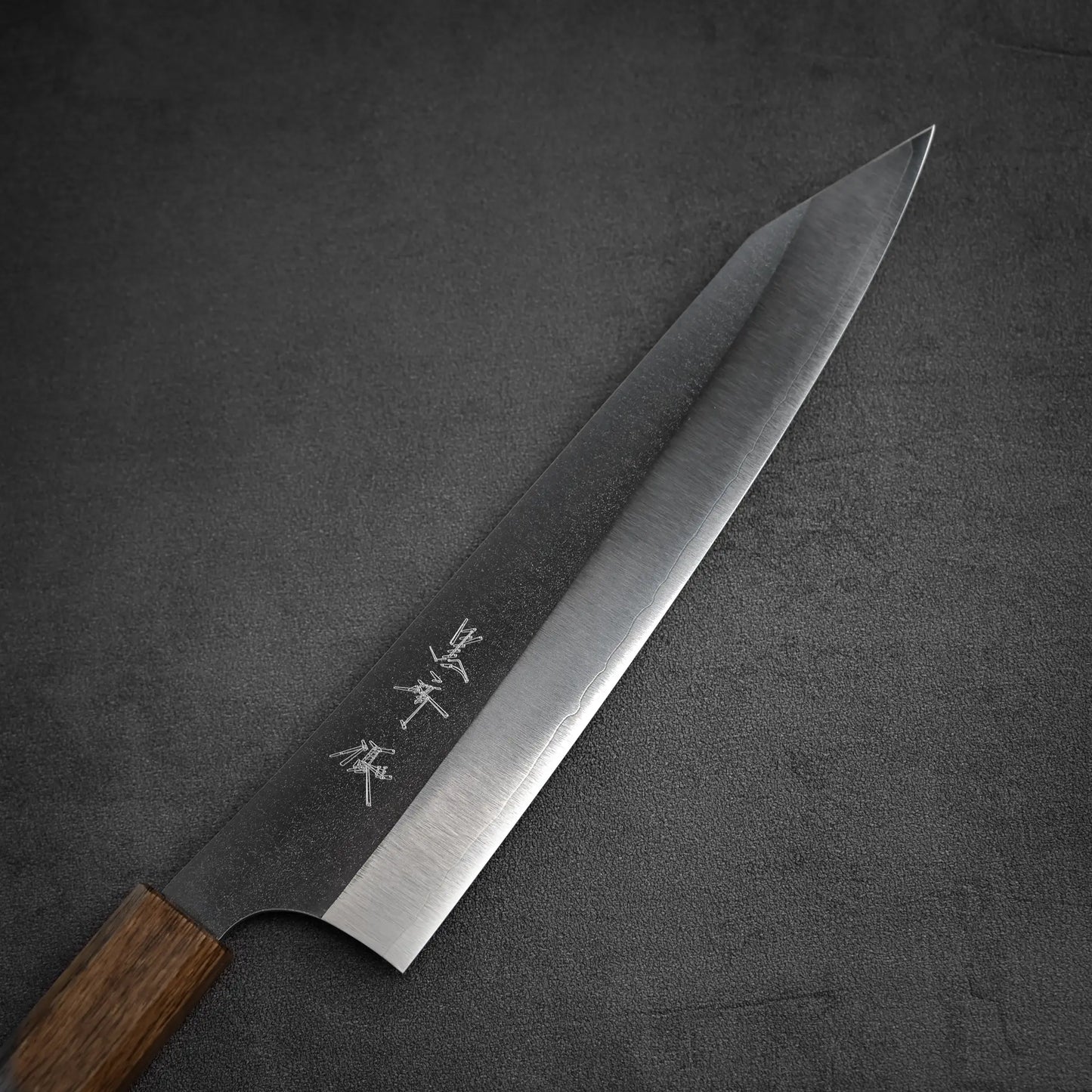 The Yu Kurosaki Gekko VG-XEOS kiritsuke gyuto 210mm features a wooden handle and a polished VG-XEOS blade with engraved Japanese characters, shown on a dark gray textured surface.