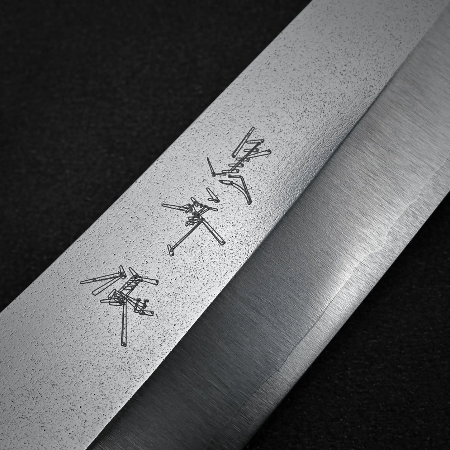 Close-up of the Yu Kurosaki Gekko VG-XEOS kiritsuke gyuto 210mm blade, featuring Japanese characters, against a dark textured background.