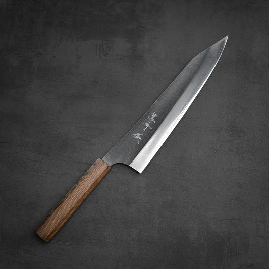A Yu Kurosaki Gekko VG-XEOS kiritsuke gyuto 240mm knife with a wooden handle and sharp, pointed blade rests on a dark textured surface.