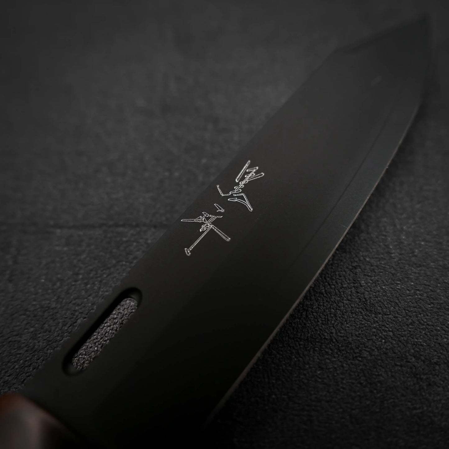 A close-up of the Yu Kurosaki SG2 folding pocket knife - ironwood shows its black stainless steel blade etched with two crossed swords and text, set against a textured dark background.