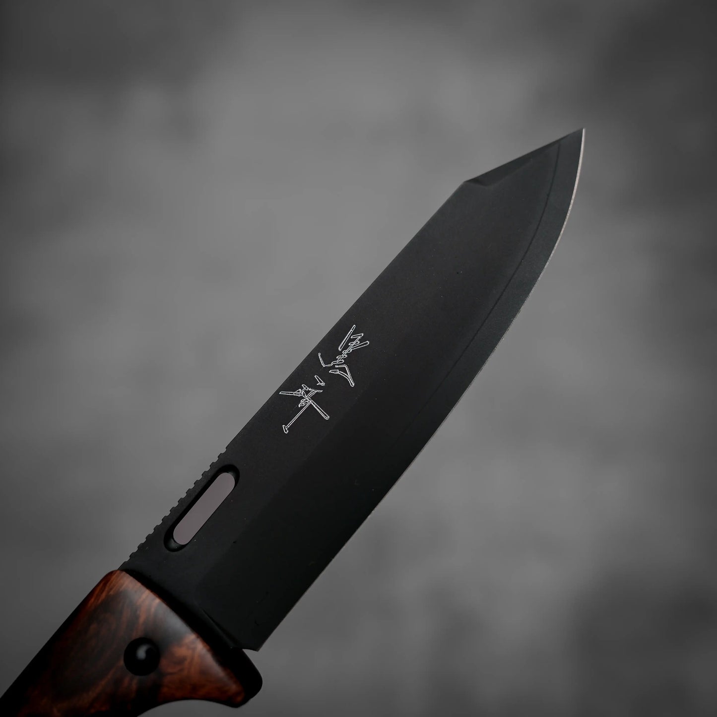 A close-up of the Yu Kurosaki SG2 folding pocket knife - ironwood, showing the engraved blade, textured handle, and a blurred grey background.