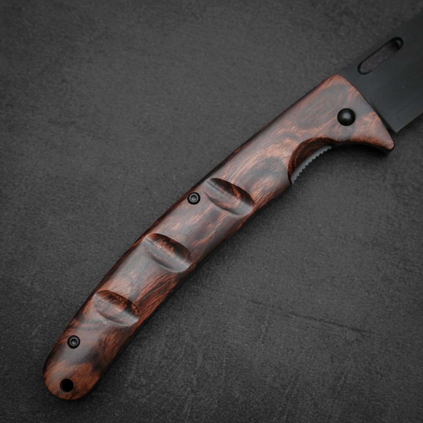 Close-up of the Yu Kurosaki SG2 folding pocket knife - ironwood, featuring a dark, polished handle with deep finger grooves. Its blade is premium SG2 stainless steel for superior edge retention, resting on a textured black surface.
