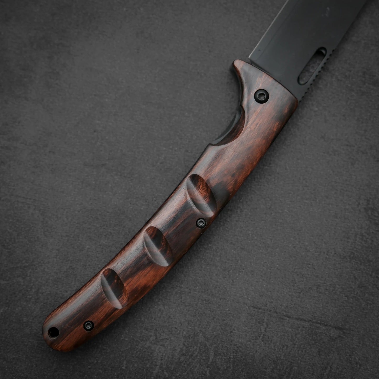Close-up of the Yu Kurosaki SG2 folding pocket knife - ironwood by Yu Kurosaki, showcasing its dark ironwood handle with finger grooves on a textured surface. The SG2 stainless steel blade is partially visible in the upper right corner.
