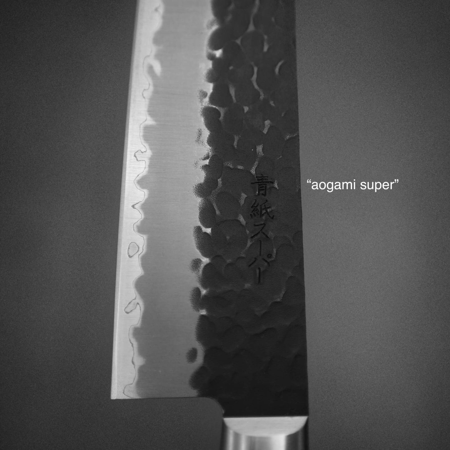Close up view of Ittosai Kotetsu tsuchime kurouchi aogami super kiritsuke gyuto showing the translated kanji. It reads aogami super