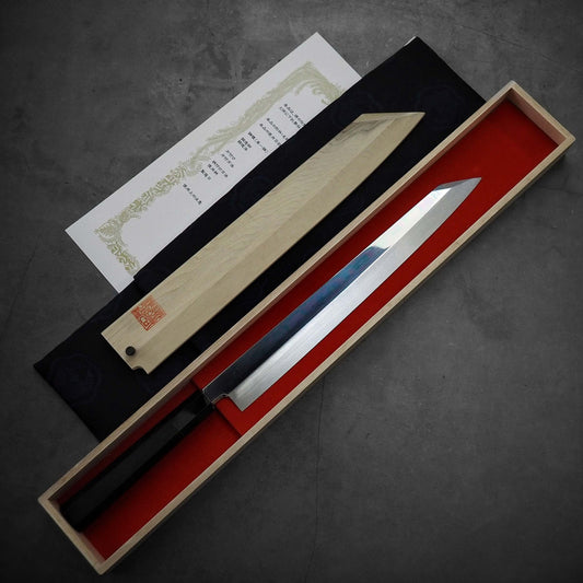 A Kenji Togashi aogami#2 honyaki kiritsuke yanagiba 300mm rests in a red-lined wooden box, with the lid and a Japanese certificate beside it on a gray surface.